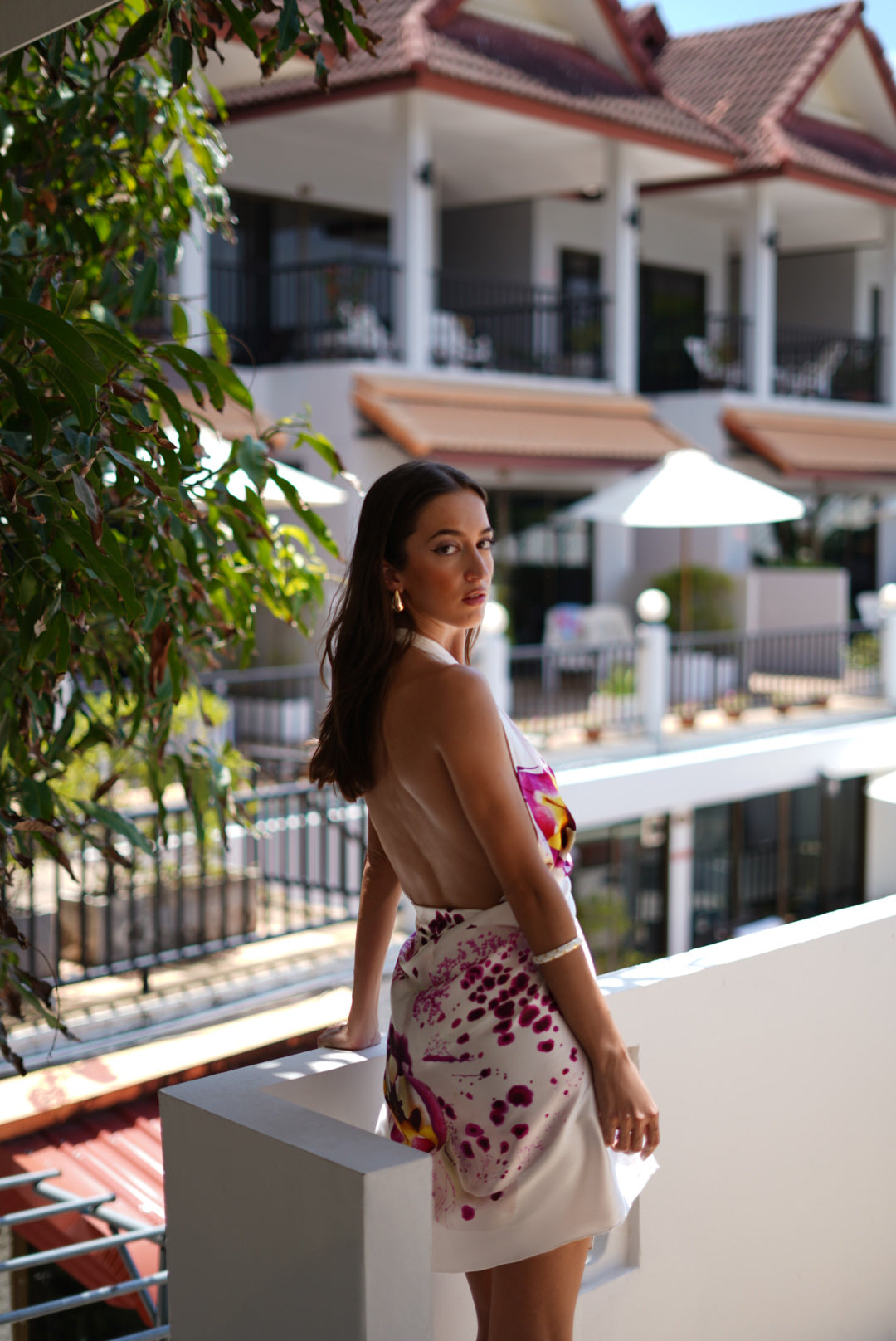 Side view of a model wearing the Bunga luxury silk sarong as an elegant backless dress on a luxury resort balcony.